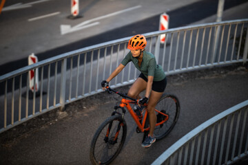 Naklejka premium Pretty, young woman with her mountain bike going for a ride past the city limits, getting the daily cardio dose
