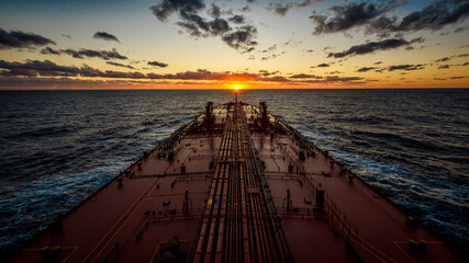 A super tanker is proceeding by ocean to sunset horizon