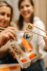 Focus on rolls. Mom and daughter are holding sushi rolls with Chinese chopsticks. Blurred background.