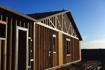 Fototapeta premium Exterior view of residential wood framing with exposed studs, sheathing panels, and roof trusses, illustrating early-phase construction and structural envelope installation