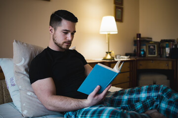 Young handsome man laying on bed,resting and reading a book