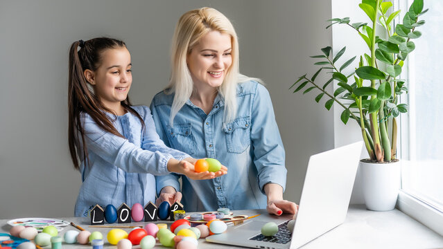 mother and daughter bloggers wearing rabbit ears headband sitting at kitchen at home. easter preparation coloring eggs together