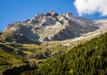 Impressive mountain in summer surrounded by green meadows with forests and steep walls