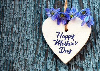 Happy Mother's Day greeting card with spring flowers and decorative heart on a blue wooden background. 