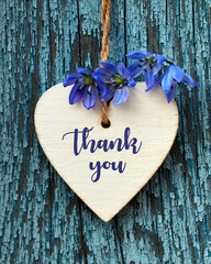 Thank You or thanks greeting card with spring flowers and decorative white heart on a blue wooden background.International Thank You Day or Mother's Day concept.