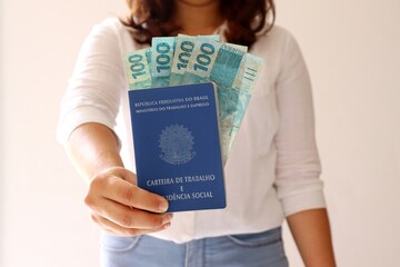 Woman holding a Brazilian Work Card (Carteira de Trabalho) and Brazilian Money.
