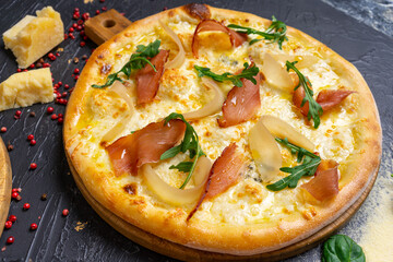 Pizza with prosciutto (parma ham), arugula (salad rocket) and parmesan on dark wooden background close up. Italian cuisine.