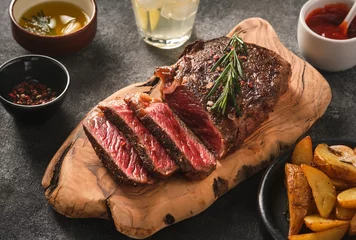 Tuinposter Sliced grilled meat steak New York Striploin with sauce and potato on wooden board on grey background. © FoodAndPhoto