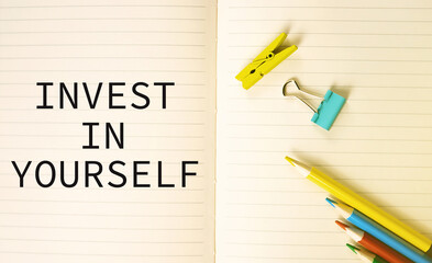 Text invest in you in a notebook with colorful pencils beside.