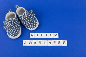 Autism Awareness background. Children's denim sports shoes with inscription Autism Awareness on blue background. Flat lay. Copy space.