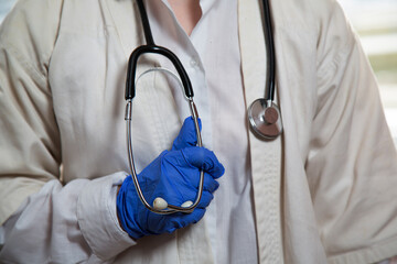 A female doctor holds a stethoscope in her hand. A doctor's hand in a blue medical glove. The female hand of a medical worker in a disposable glove. Close up.
