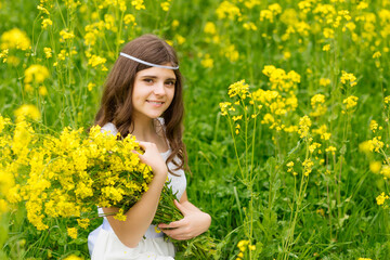 Naklejka na ściany i meble Beautiful girl in a rapeseed field. A child in a blooming field with yellow flowers. Plantation of yellow flowers