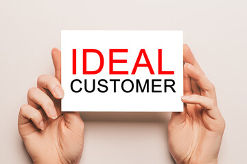 Female hands hold card paper with text IDEAL CUSTOMER on a yellow background. Business and finance concept