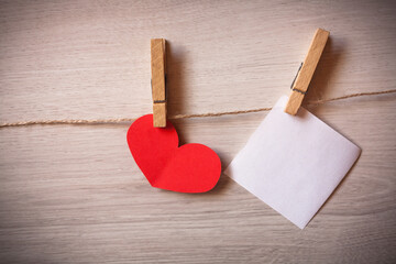 Clothespins with blank sheets of paper hanging on wooden background with hearts.
