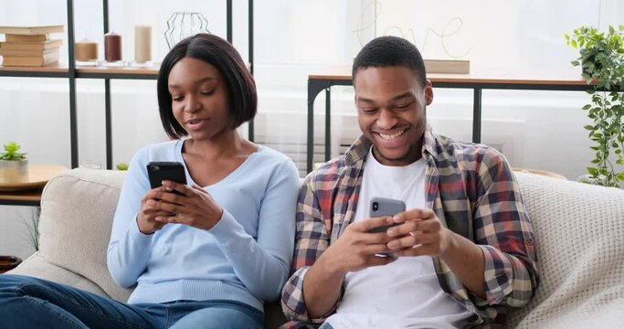 Couple using mobile phones sitting on sofa at home