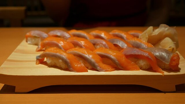 Wooden plate fool of salmon nigiri sushi, tasty meal in Japanese restaurant. Many pieces of Chutoro harami close up shot, woman pick up one item using chopsticks