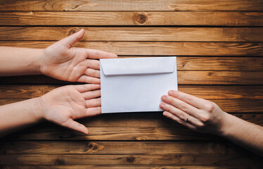 White small envelope (letter) in the hands of two people on brown wooden background. The concept of...
