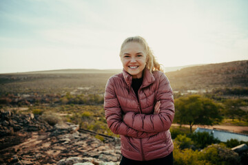 Caucasian female smiling while hiking on mountain trail standing crossed armed