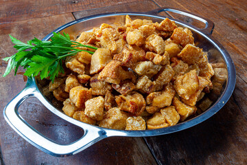 pork rinds (torresmo) fried in ceramic bowl on rustic wooden table in restaurant.