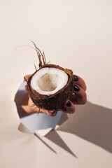 A hand holds a broken coconut through a hole in the paper. Hard Light. Copy space.