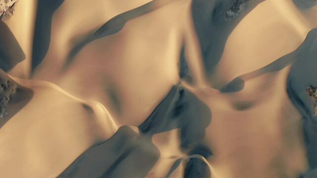Aerial view of a drone flying over beautiful massive golden sand dunes on sunset. 4K top-down view on the amazing wavy patterns on the desert earth. Road trip to the desert nature, California, USA