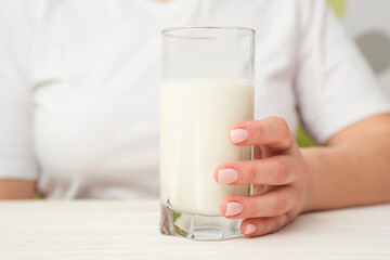 Woman with a glass of milk sits at a white wooden table. Healthy eating. Healthy lifestyle