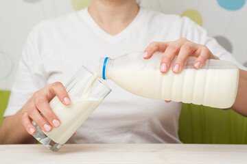 Fototapeta na wymiar A woman is pouring milk from plastic bottle in a glass. Healthy diet