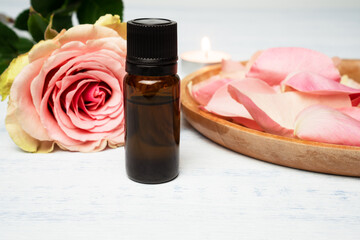Aromatherapy composition. Bottle of rose essential oil with rose bud, rose petals and burning candle.