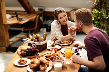 Happy woman feeding her boyfriend during breakfast at dining table.
