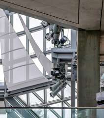 Daytime view of spotlights and lighting fixtures hanging from supports in a concrete atrium nobody