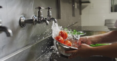 Caucasian female chef washing vegetables in colander in restaurant kitchen