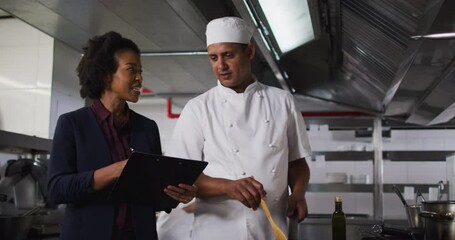 African american female manager holding clipboard and talking with chef