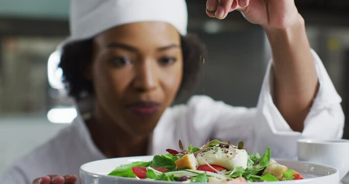 African american female chef garnishing dish and similing in restaurant kitchen