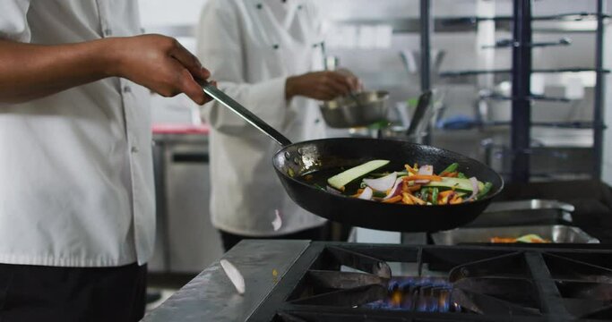 Midsection of mixed race male chef frying vegetables in pan