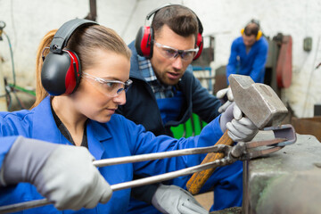 workers shaping metal with hammer over anvil