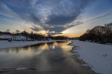Winter sunset over the river. Old town by the river. Winter landscape and evening sky.