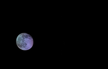 Waning multicolored moon on a dark sky. Moon with craters, isolated on black background.