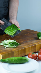 Close up of Chef cook hands chopping vegetables for traditional Asian cuisine with Japanese knife. Professional Sushi chef cutting cucumber for rolls.