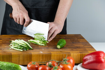 Close up of Chef cook hands chopping vegetables for traditional Asian cuisine with Japanese knife. Professional Sushi chef cutting cucumber for rolls.