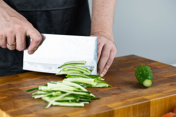 Close up of Chef cook hands chopping vegetables for traditional Asian cuisine with Japanese knife. Professional Sushi chef cutting cucumber for rolls.