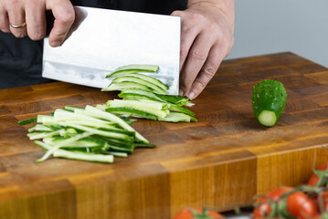 Close up of Chef cook hands chopping vegetables for traditional Asian cuisine with Japanese knife. Professional Sushi chef cutting cucumber for rolls.
