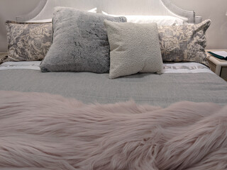 a cleanly made pink, white, and grey bed, topped with throw pillows and a fluffy blanket