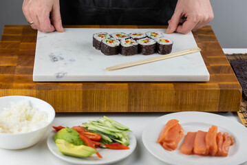 Closeup of chef hands preparing japanese food. Professional chef making sushi at restaurant. Man hands making traditional asian sushi rolls on cutting board.