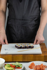 Closeup of chef hands preparing japanese food. Professional chef making sushi at restaurant. Man hands making traditional asian sushi rolls on cutting board.