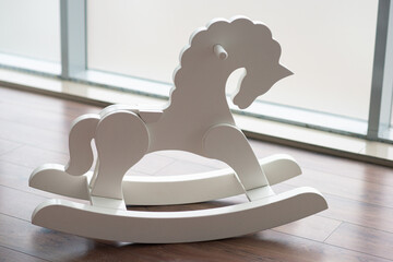 white wooden baby rocking horse stands on the floor near a large window