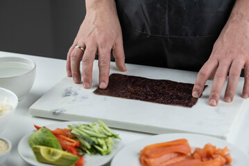 Closeup of chef hands preparing japanese food. Professional chef making sushi at restaurant. Man hands making traditional asian sushi rolls on cutting board.