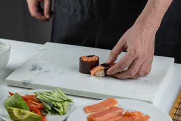 Closeup of chef hands preparing japanese food. Professional chef making sushi at restaurant. Man hands making traditional asian sushi rolls on cutting board.