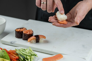 Closeup of chef hands preparing japanese food. Professional chef making sushi at restaurant. Man hands making traditional asian sushi rolls on cutting board.