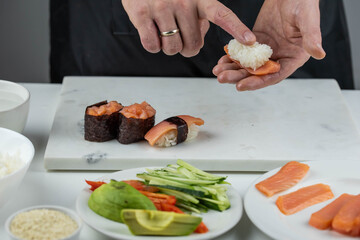 Closeup of chef hands preparing japanese food. Professional chef making sushi at restaurant. Man hands making traditional asian sushi rolls on cutting board.