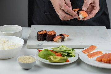 Closeup of chef hands preparing japanese food. Professional chef making sushi at restaurant. Man hands making traditional asian sushi rolls on cutting board.